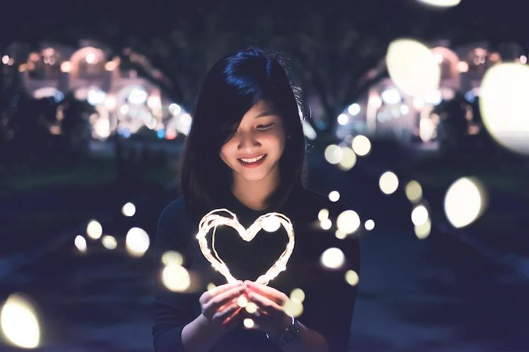 Smiling woman holding heart made of lights.