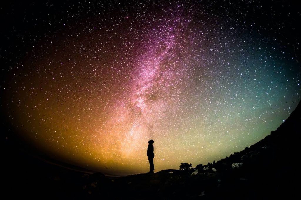 Person looking up at the colorful night sky with the Milky Way in the background.