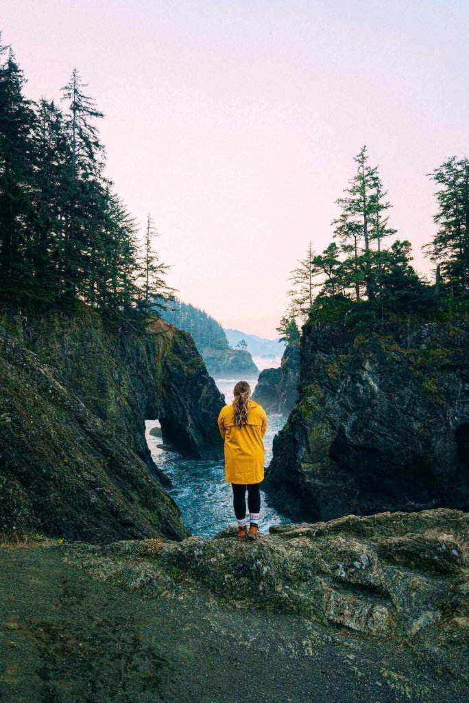 Woman in raincoat standing in front of some rocks and water.