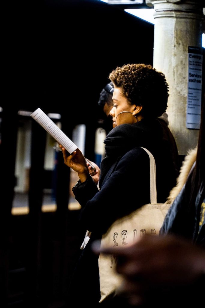 Standing woman reading a book while waiting for a train.