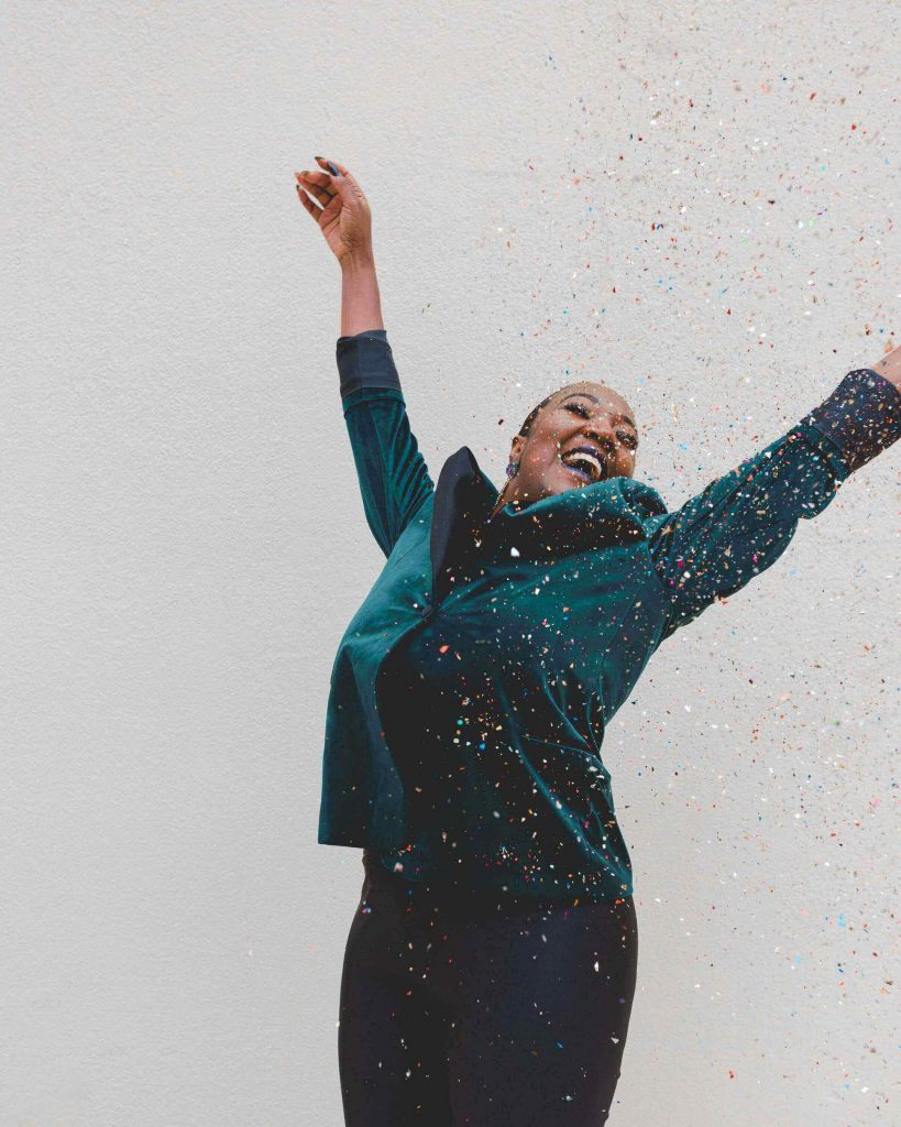 A woman raises her arms in the air as confetti rains down.